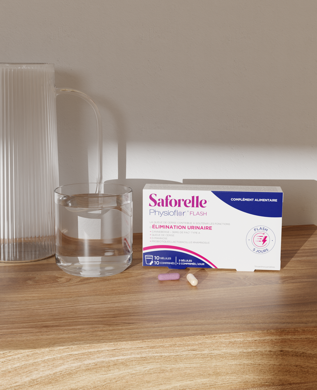 Boîte Saforelle Physioflor Flash avec un verre d’eau et comprimés sur une table, complément alimentaire pour le confort urinaire